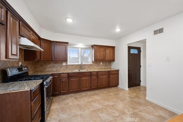 kitchen featuring decorative backsplash, light stone counters, stainless steel range with gas stovetop, and sink