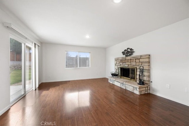 unfurnished living room featuring dark wood-type flooring, a wealth of natural light, and a stone fireplace