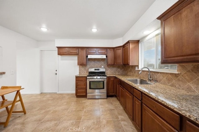 kitchen with backsplash, light stone counters, stainless steel range with gas cooktop, and sink