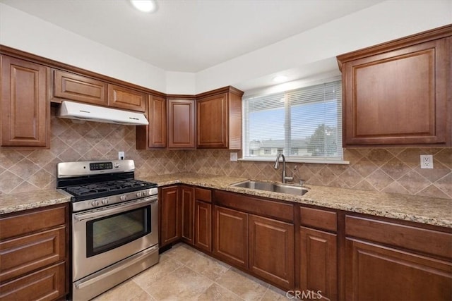 kitchen featuring gas range, backsplash, light stone counters, and sink