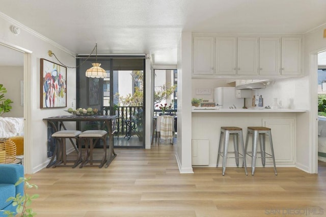 kitchen featuring a kitchen breakfast bar, white cabinets, ornamental molding, white refrigerator, and light hardwood / wood-style flooring