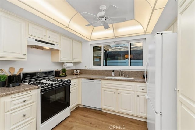 kitchen featuring a tray ceiling, sink, ceiling fan, light hardwood / wood-style floors, and white appliances