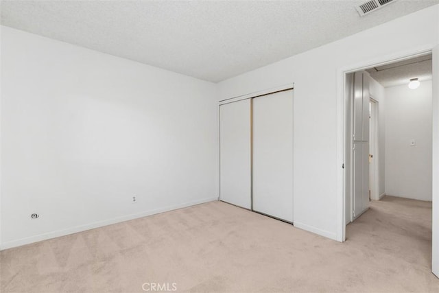 unfurnished bedroom featuring light carpet, a textured ceiling, and a closet