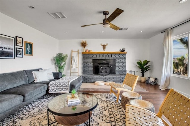 living room with ceiling fan, a wood stove, and wood-type flooring