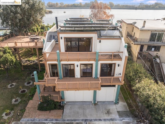 back of property with a water view, a balcony, and a garage