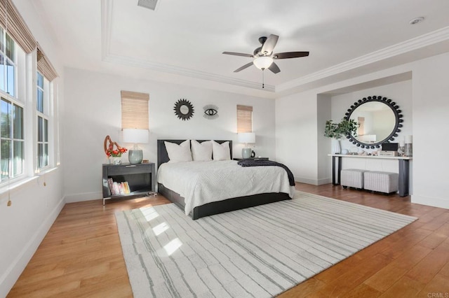 bedroom with ceiling fan, a tray ceiling, ornamental molding, and light hardwood / wood-style floors