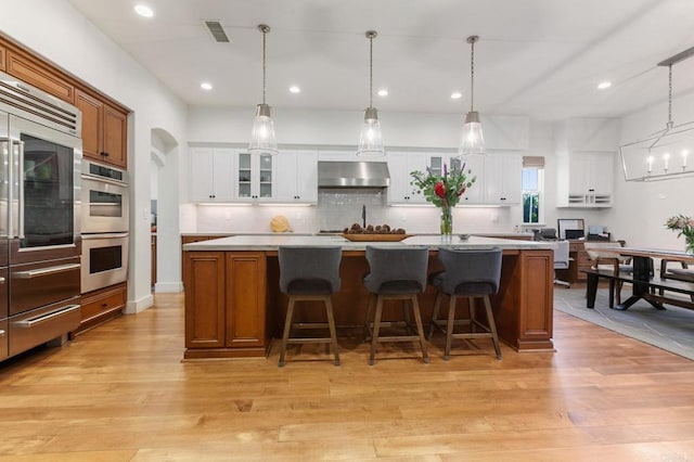 kitchen with decorative light fixtures, white cabinetry, and wall chimney range hood