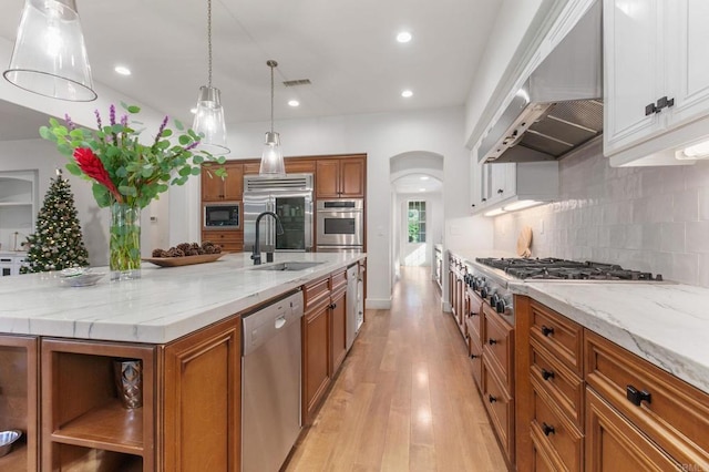 kitchen featuring sink, white cabinets, built in appliances, and wall chimney range hood