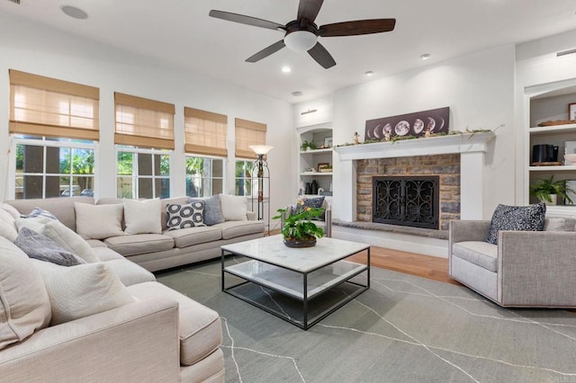 living room featuring ceiling fan, wood-type flooring, built in features, and a fireplace