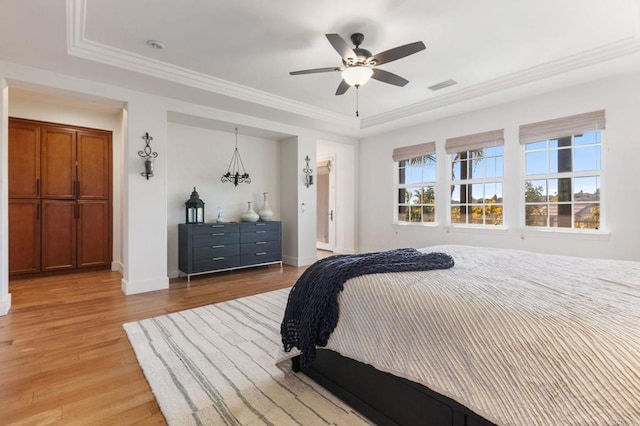 bedroom with ceiling fan, a tray ceiling, crown molding, and light wood-type flooring