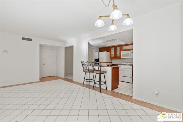 kitchen featuring decorative light fixtures, an inviting chandelier, white appliances, a breakfast bar area, and light tile patterned floors