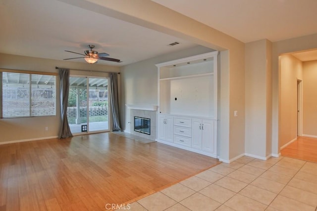 unfurnished living room with ceiling fan, a tiled fireplace, and light wood-type flooring