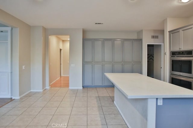 kitchen with gray cabinets, light tile patterned flooring, a center island, and stainless steel double oven