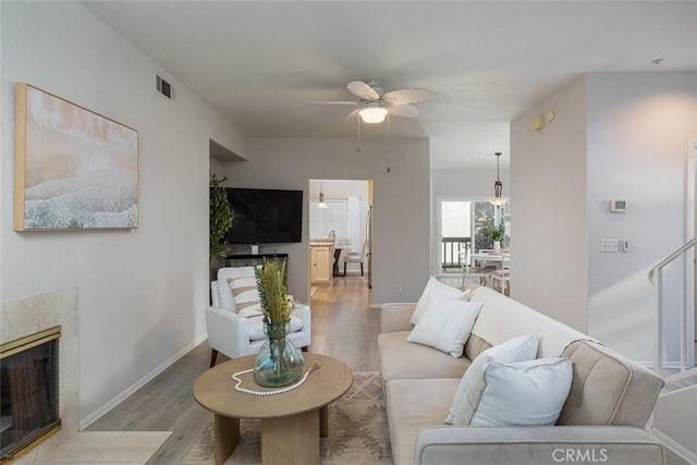 living room featuring light wood-type flooring, ceiling fan, and a fireplace