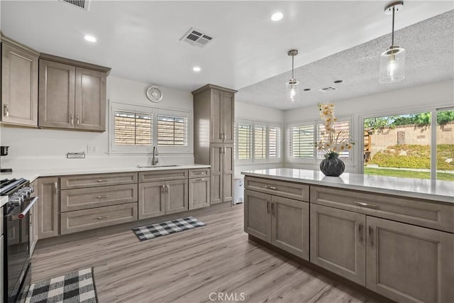 kitchen featuring decorative light fixtures, light hardwood / wood-style floors, sink, a textured ceiling, and range