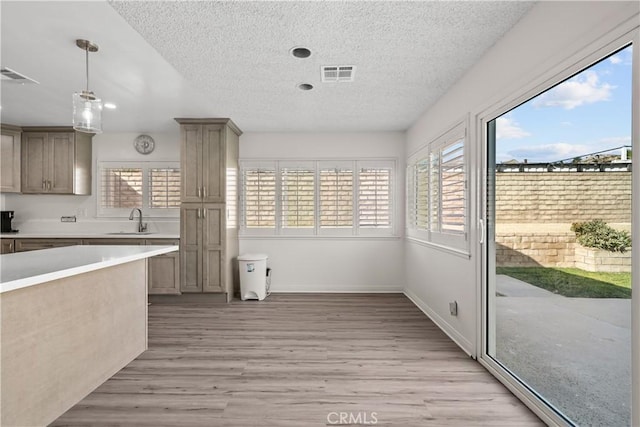 kitchen featuring decorative light fixtures, sink, a textured ceiling, and light hardwood / wood-style flooring