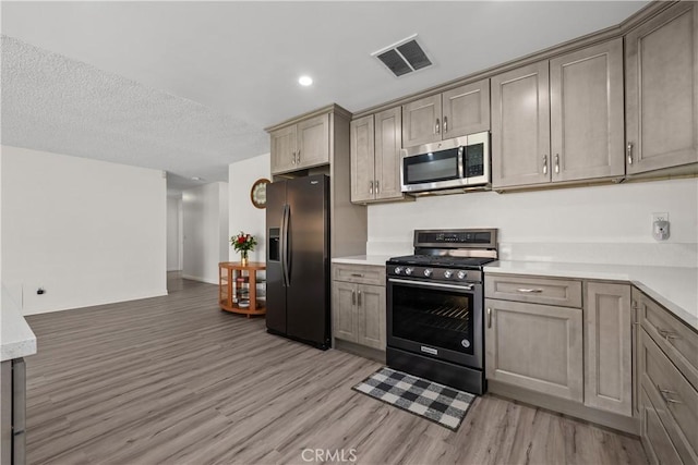 kitchen with a textured ceiling, stainless steel appliances, and light hardwood / wood-style flooring