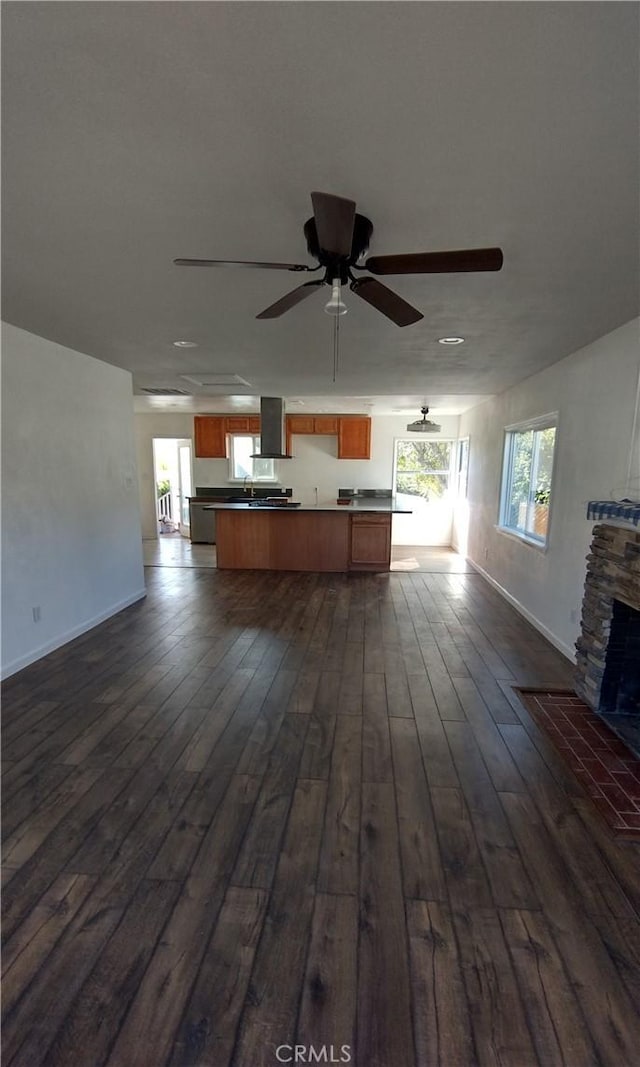 unfurnished living room featuring a stone fireplace, dark hardwood / wood-style floors, and ceiling fan