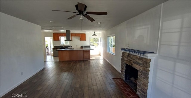 unfurnished living room with a stone fireplace, dark hardwood / wood-style floors, and ceiling fan