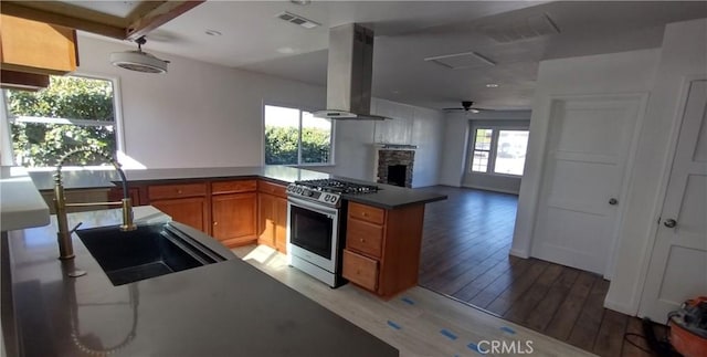 kitchen with sink, light hardwood / wood-style floors, island exhaust hood, a stone fireplace, and stainless steel range with gas cooktop