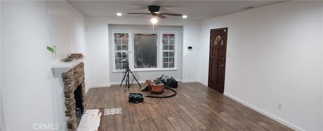 interior space with dark hardwood / wood-style floors, ceiling fan, and a stone fireplace