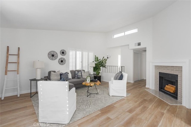 living room featuring a high ceiling, a brick fireplace, and light hardwood / wood-style flooring