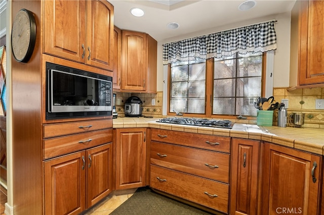 kitchen with tile counters, decorative backsplash, stainless steel gas stovetop, and black microwave