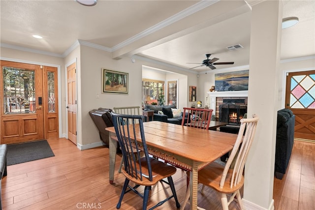 dining space featuring ceiling fan, ornamental molding, a stone fireplace, and light wood-type flooring