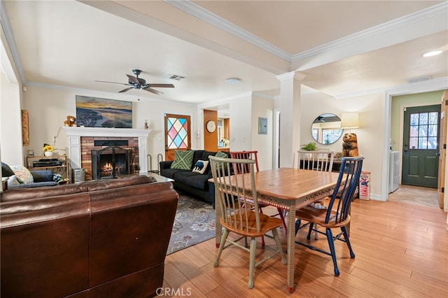 dining room with a brick fireplace, light hardwood / wood-style floors, crown molding, and ceiling fan