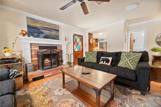 living room featuring ceiling fan, hardwood / wood-style floors, crown molding, and a fireplace