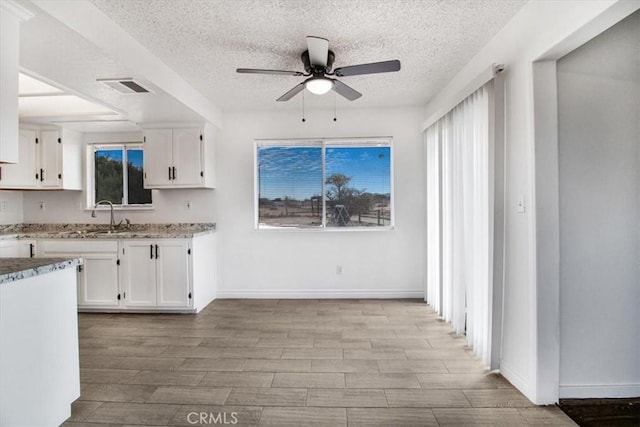 kitchen with a textured ceiling, white cabinetry, sink, ceiling fan, and light stone counters