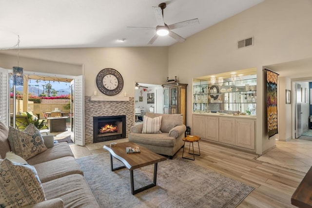 living room with ceiling fan, vaulted ceiling, a tile fireplace, and light wood-type flooring