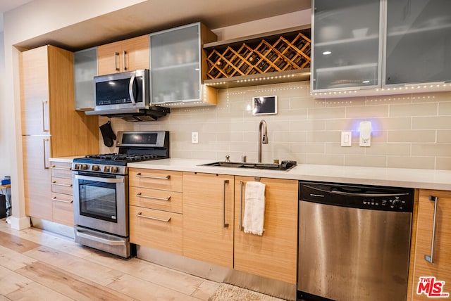 kitchen with light wood-type flooring, stainless steel appliances, decorative backsplash, and sink