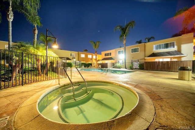 pool at night featuring a community hot tub and a patio area