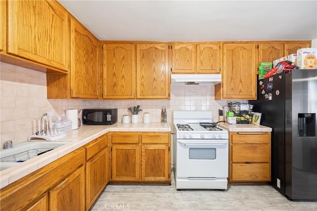 kitchen featuring white gas range oven, backsplash, tile countertops, and stainless steel fridge with ice dispenser