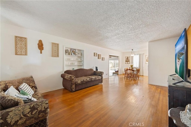 living room featuring built in shelves, hardwood / wood-style flooring, and a textured ceiling