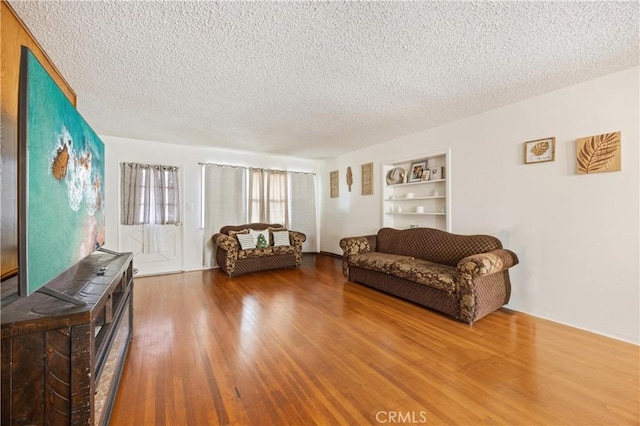 living room with built in features, hardwood / wood-style floors, and a textured ceiling