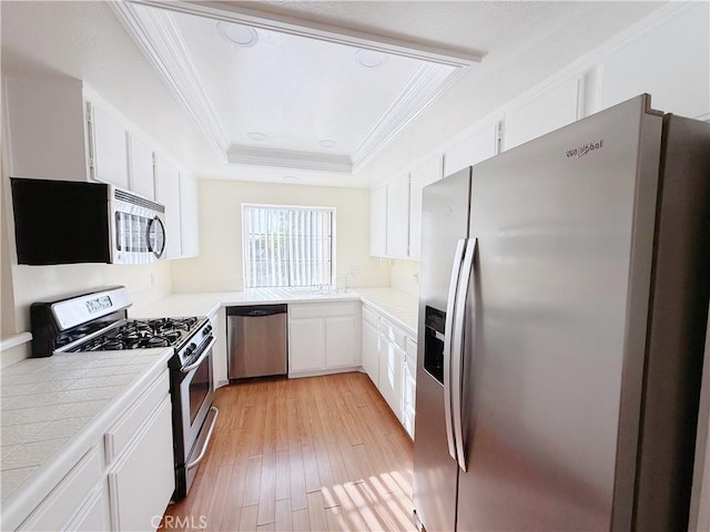 kitchen with a tray ceiling, white cabinetry, light hardwood / wood-style flooring, appliances with stainless steel finishes, and tile counters