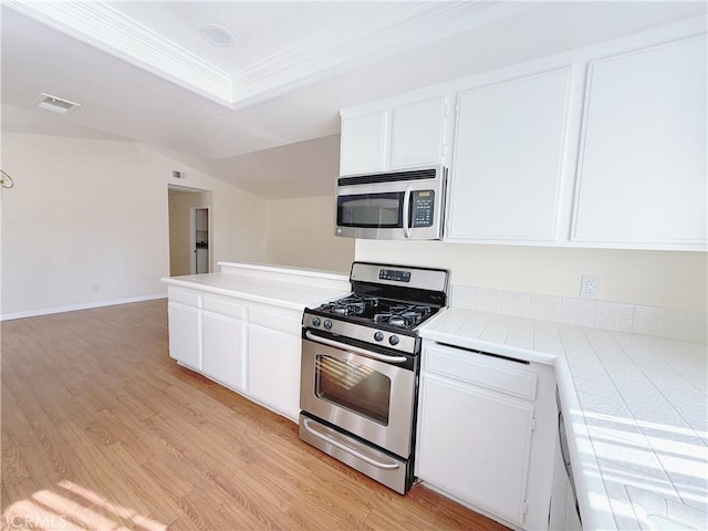 kitchen featuring tile countertops, crown molding, white cabinetry, light hardwood / wood-style flooring, and stainless steel appliances