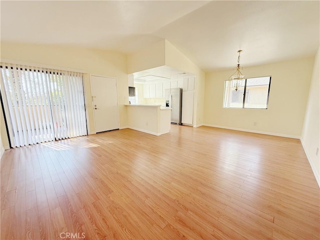 unfurnished living room with light hardwood / wood-style flooring, a healthy amount of sunlight, a notable chandelier, and vaulted ceiling