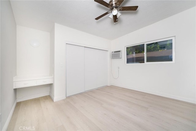 unfurnished bedroom with ceiling fan, a closet, a wall unit AC, and light hardwood / wood-style flooring