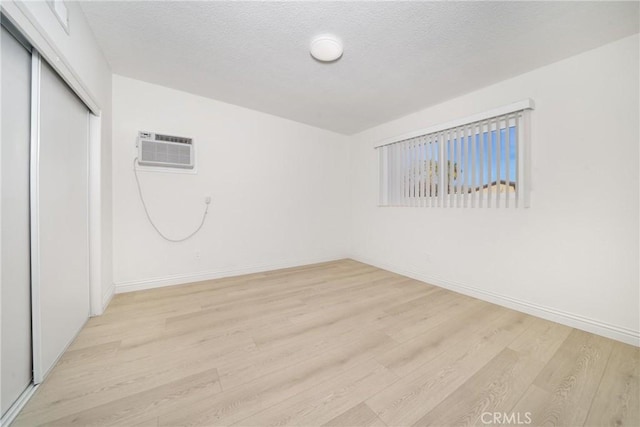 empty room featuring light hardwood / wood-style floors, a textured ceiling, and a wall unit AC