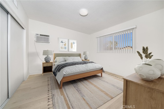 bedroom with light wood-type flooring, a closet, a textured ceiling, and a wall unit AC