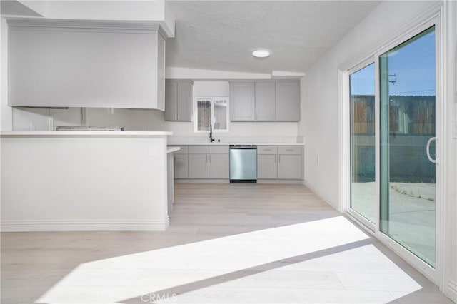 kitchen with lofted ceiling, gray cabinets, light hardwood / wood-style floors, stainless steel dishwasher, and sink