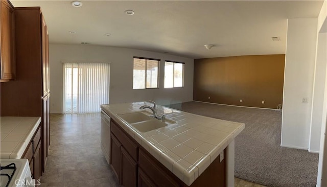 kitchen featuring dishwasher, tile countertops, a center island with sink, sink, and range