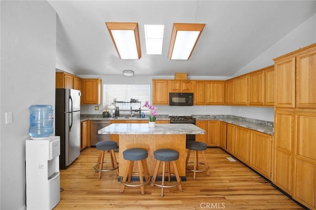kitchen with vaulted ceiling, a center island, a kitchen bar, light hardwood / wood-style flooring, and stainless steel appliances