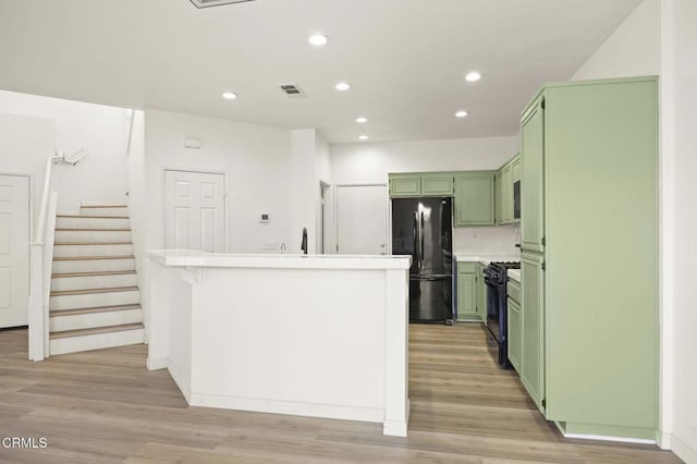 kitchen featuring decorative backsplash, light wood-type flooring, green cabinetry, black appliances, and sink