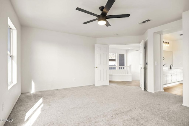 unfurnished bedroom with ceiling fan, sink, light colored carpet, and ensuite bath