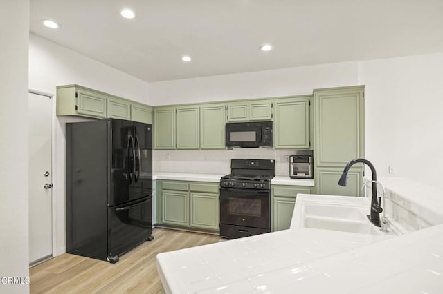 kitchen featuring black appliances, sink, kitchen peninsula, light wood-type flooring, and green cabinets