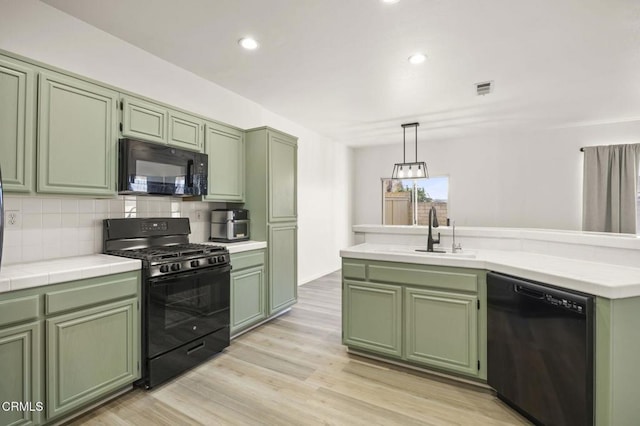 kitchen featuring backsplash, black appliances, sink, green cabinets, and hanging light fixtures